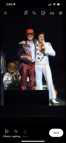 Elton Dan standing side-by-side on stage with an Elvis tribute artist, who is speaking into a microphone.