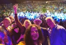 Guitarist taking a selfie of the band with a large crowd in the background.