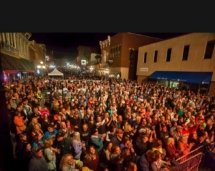 A photo of the crowd at a nighttime street concert. People fill a few blocks with shops and restaurants on either side.