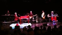 A nice landscape shot of the full band on stage. The first couple of rows of fans is visible.