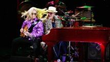 Dan at his red piano, wearing a leopard-print coat. His guitarist is rocking out next to him on the piano bench.