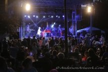 Elton Dan and the Rocket Band on stage at an outdoor concert. It's night and the crowd is on their feet in front of the stage.