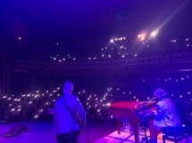 A shot from the stage with Dan on the right, the bass player in the middle, and the crowd in the background with their phone lights on.