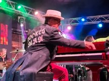 Elton Dan at his red piano, reaching for a high note with his right hand. He's wearing a black coat with tails that says, "Rocket Man" on the back.