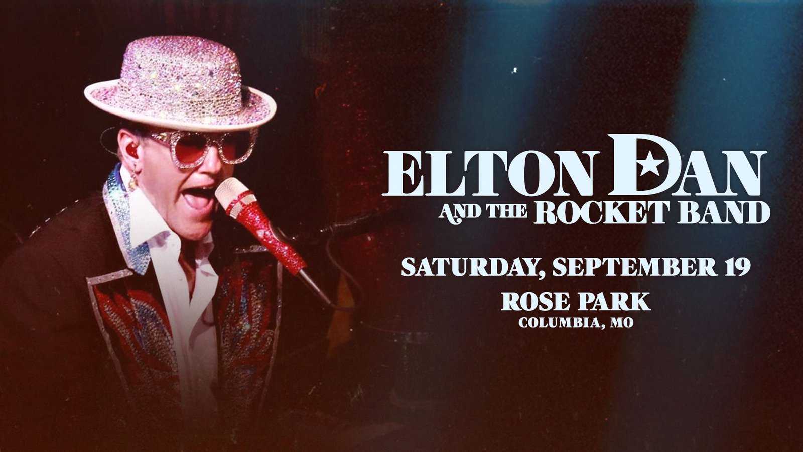 A shot of Elton Dan and the Rocket band on stage with the crowd in the foreground. White lights are shining beams of light in all directions from the stage.